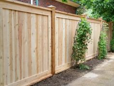 a wooden fence next to a brick building and trees in the background with green leaves growing on it