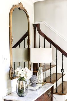 a vase with flowers sitting on top of a table next to a mirror and stairs