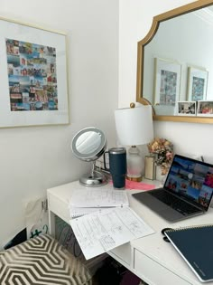 a laptop computer sitting on top of a white desk next to a mirror and lamp