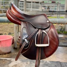 a brown saddle is hanging on a fence