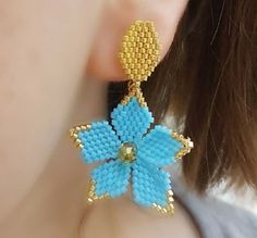 a close up of a person's ear wearing blue and gold beaded earrings