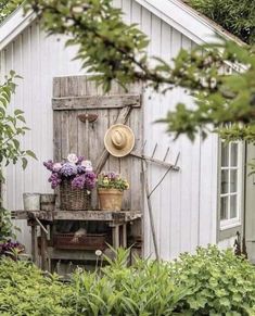 a garden shed with flowers and a hat on the top of it's door