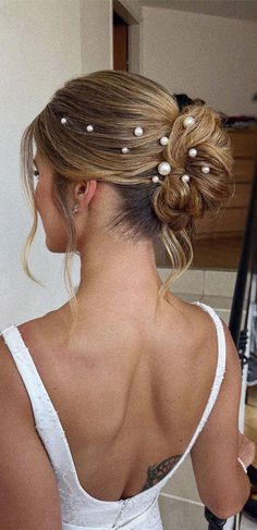 a woman with her back to the camera, wearing a white dress and pearls in her hair