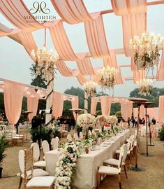 the tables are set up with white flowers and chandeliers for an outdoor wedding