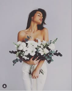 a woman with flowers in her hands is posing for the camera while wearing white pants