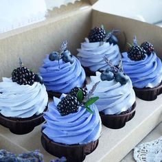 several cupcakes with blue icing and blackberries on top in a box