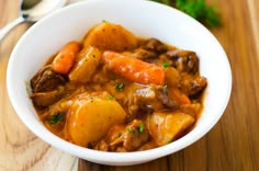 a white bowl filled with stew and carrots on top of a wooden cutting board