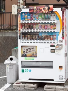 a white vending machine sitting on the side of a road next to a trash can