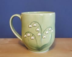 a green coffee cup with white flowers on the inside sits on a wooden table in front of a blue wall