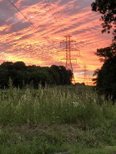 the sun is setting behind power lines in an open field with tall grass and trees