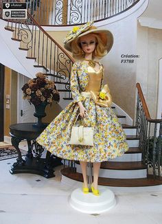 a barbie doll wearing a yellow dress and matching hat stands in front of a spiral staircase