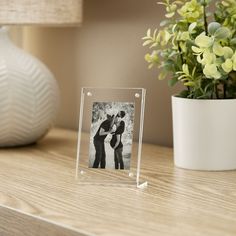 a small clear photo frame sitting on top of a wooden table next to a potted plant