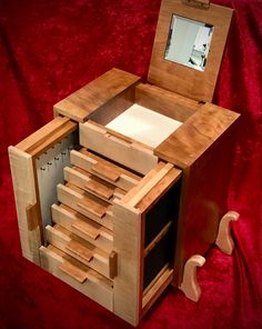 a wooden jewelry box with drawers and mirror on red velvet covered tableclothed area