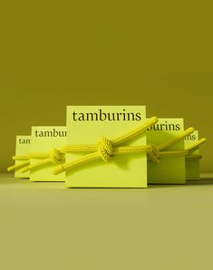 three yellow tags tied to each other in front of a green background with the word tamburins written on them