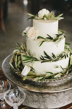 a wedding cake with white flowers and greenery on top sits on a silver platter