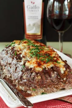 a piece of meat sitting on top of a white plate next to a glass of wine