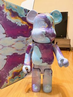 a purple and blue bear sitting on top of a hard wood floor next to a painting