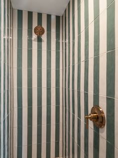 a bathroom with green and white stripes on the walls, shower head and hand held faucet