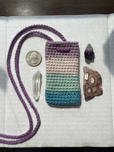 a crocheted purse and other items are on a white cloth with a purple cord