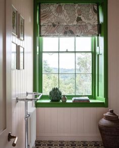 a green window in a white bathroom with a book and vase sitting on the windowsill