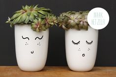 two planters with faces painted on them are sitting on a wooden table next to each other