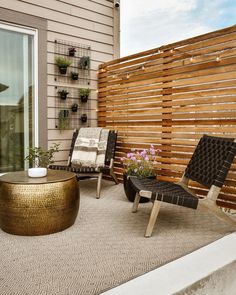 two chairs and a coffee table on a small patio with wood slats in the background