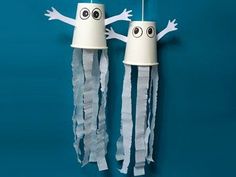 two white lamps with faces and arms made out of tissue paper on a blue wall