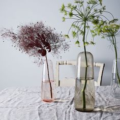 three vases filled with flowers sitting on top of a white tablecloth covered table