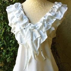 a white dress with ruffles on the shoulders and neckline is displayed in front of a bush