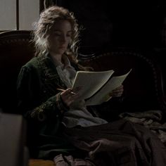 a woman sitting on top of a bed reading a book while holding a pen and paper