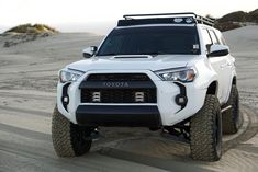 the front end of a white four - doored suv driving through sand dunes