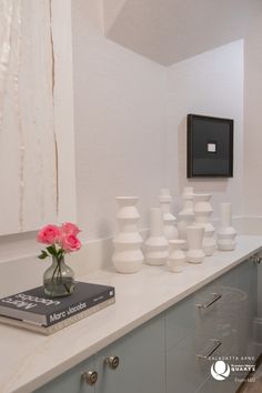 vases and flowers on a counter in a room with white walls, flooring and cabinets