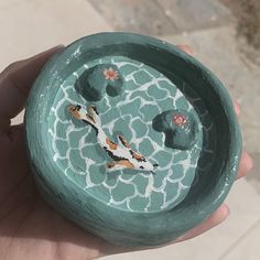 a hand holding a green bowl with fish and flowers on it