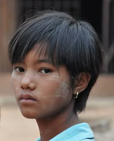 a young boy with black hair and white paint on his face looking at the camera