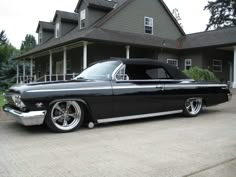 an old black car parked in front of a house with white rims and chrome wheels