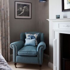 a blue chair sitting in front of a fire place next to a window with curtains