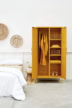 a yellow cabinet in a bedroom next to a bed and wicker baskets on the wall