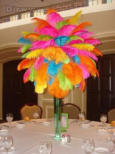 a tall vase filled with colorful feathers sitting on top of a white table cloth covered table