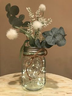 a mason jar filled with flowers and greenery on a wooden table in front of a brown wall