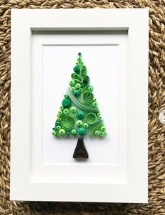 a small green christmas tree made out of buttons in a white frame on a woven mat