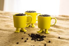 three yellow mugs filled with black beans on top of a bed next to each other