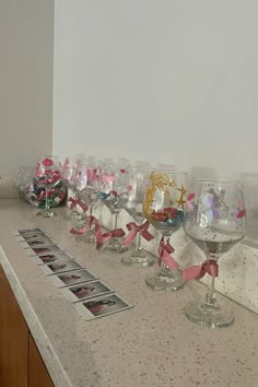 there are many wine glasses lined up on the counter with pink bows and ribbons around them