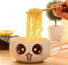 a person is eating noodles with chopsticks in a bowl on a table next to a potted plant