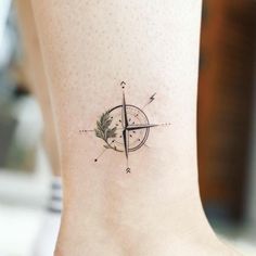 a small compass tattoo on the ankle with a green leaf and arrow in it's center