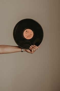 a hand holding an old vinyl record in it's left arm, against a beige background