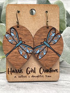 two wooden earrings with dragonflies on them and the words, harry's girl creations