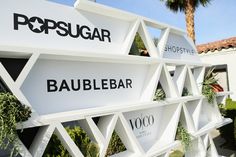 a sign that says popsugar and baublebar in front of a palm tree