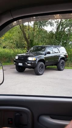 a black truck parked in a parking lot next to another vehicle with large tires on it