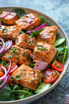 a salad with salmon, onions and tomatoes in a white bowl on top of a table