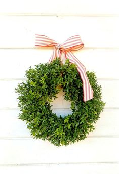 a wreath hanging on the side of a white wall with a red and white bow